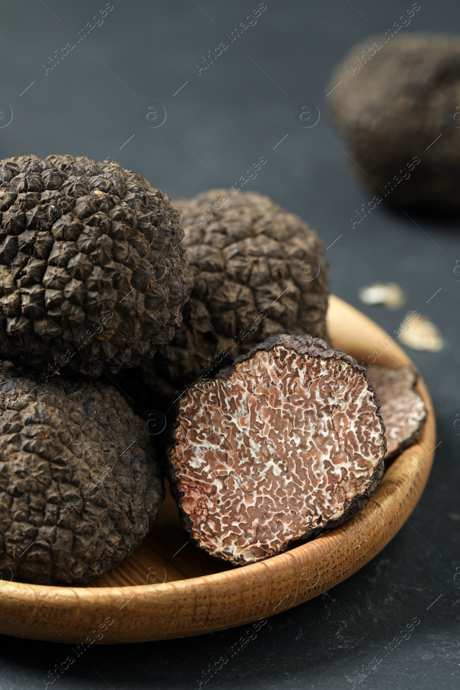 Photo of Black truffles in wooden plate on grey table, closeup