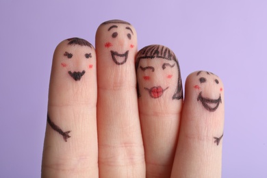 Photo of Four fingers with drawings of happy faces on violet background