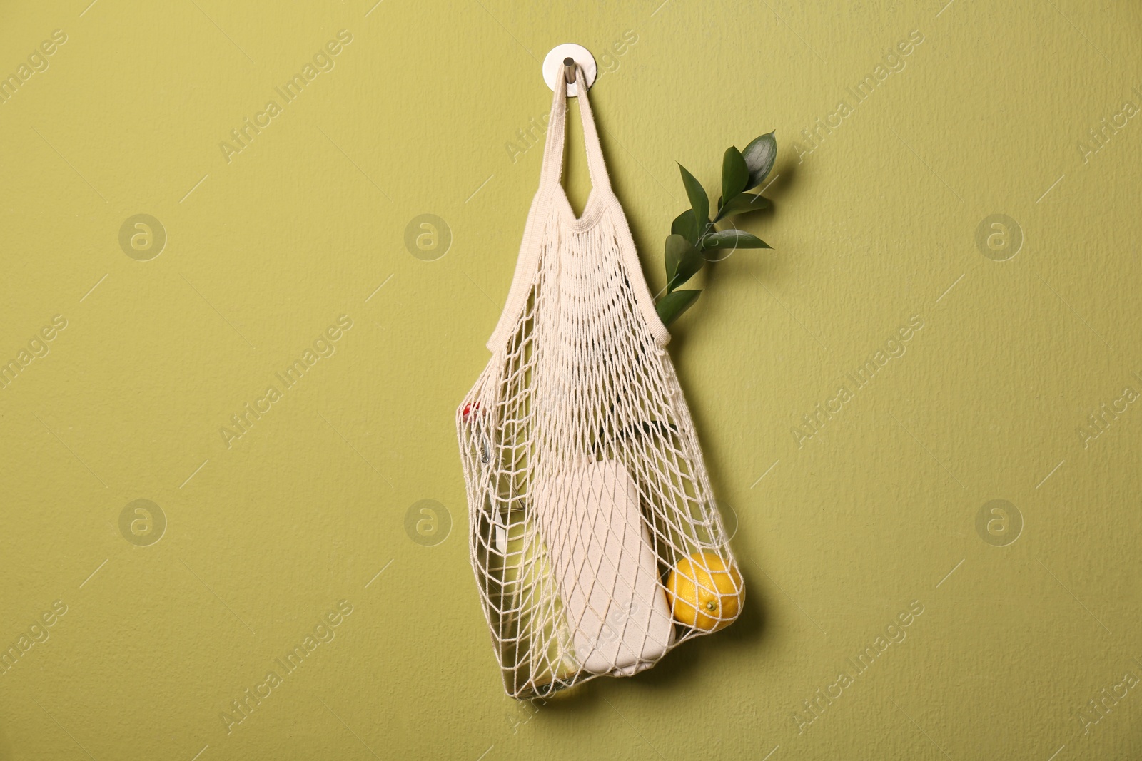 Photo of Conscious consumption. Net bag with eco friendly products hanging on olive wall, space for text