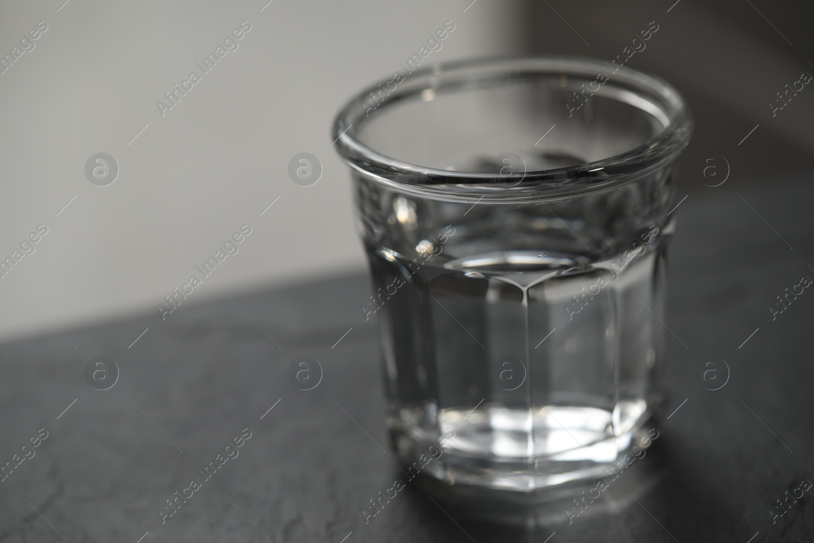 Photo of Glass of pure water on black table against blurred background, space for text