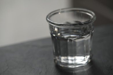 Glass of pure water on black table against blurred background, space for text