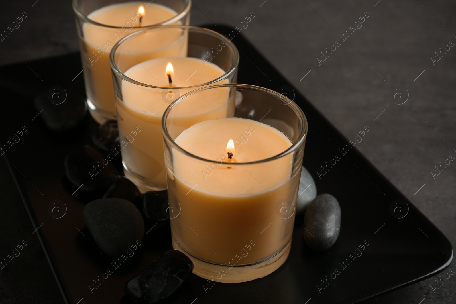 Photo of Dark plate with three burning candles and rocks on table