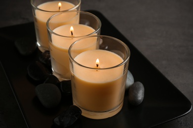 Dark plate with three burning candles and rocks on table