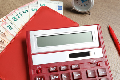 Photo of Calculator, notebook, money and alarm clock on wooden table, closeup. Tax accounting