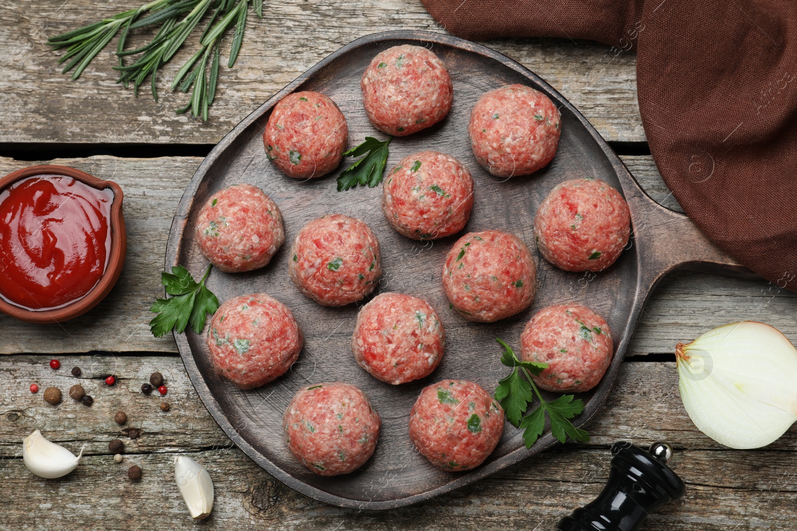 Photo of Many fresh raw meatballs and ketchup on wooden table, flat lay