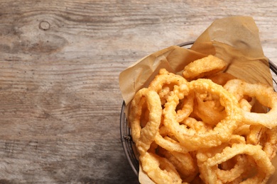 Homemade crunchy fried onion rings in wire basket on wooden background, top view. Space for text