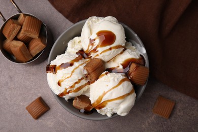 Scoops of ice cream with caramel sauce and candies on textured table, flat lay