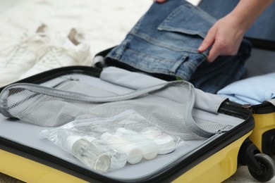 Photo of Woman with jeans packing suitcase, focus on cosmetic travel kit. Bath accessories