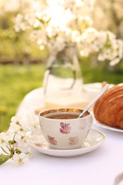 Stylish table setting with beautiful spring flowers, tea and croissants in garden