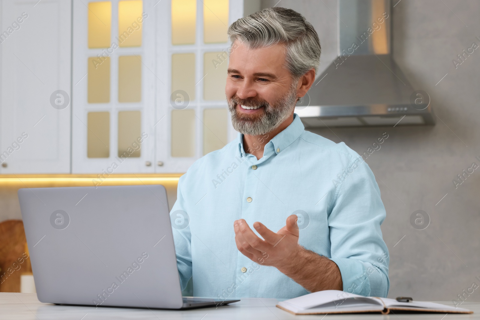Photo of Man waving hello during video chat via laptop at home