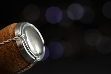 Photo of Sparkling wine cork with muselet cap against blurred festive lights, closeup. Space for text