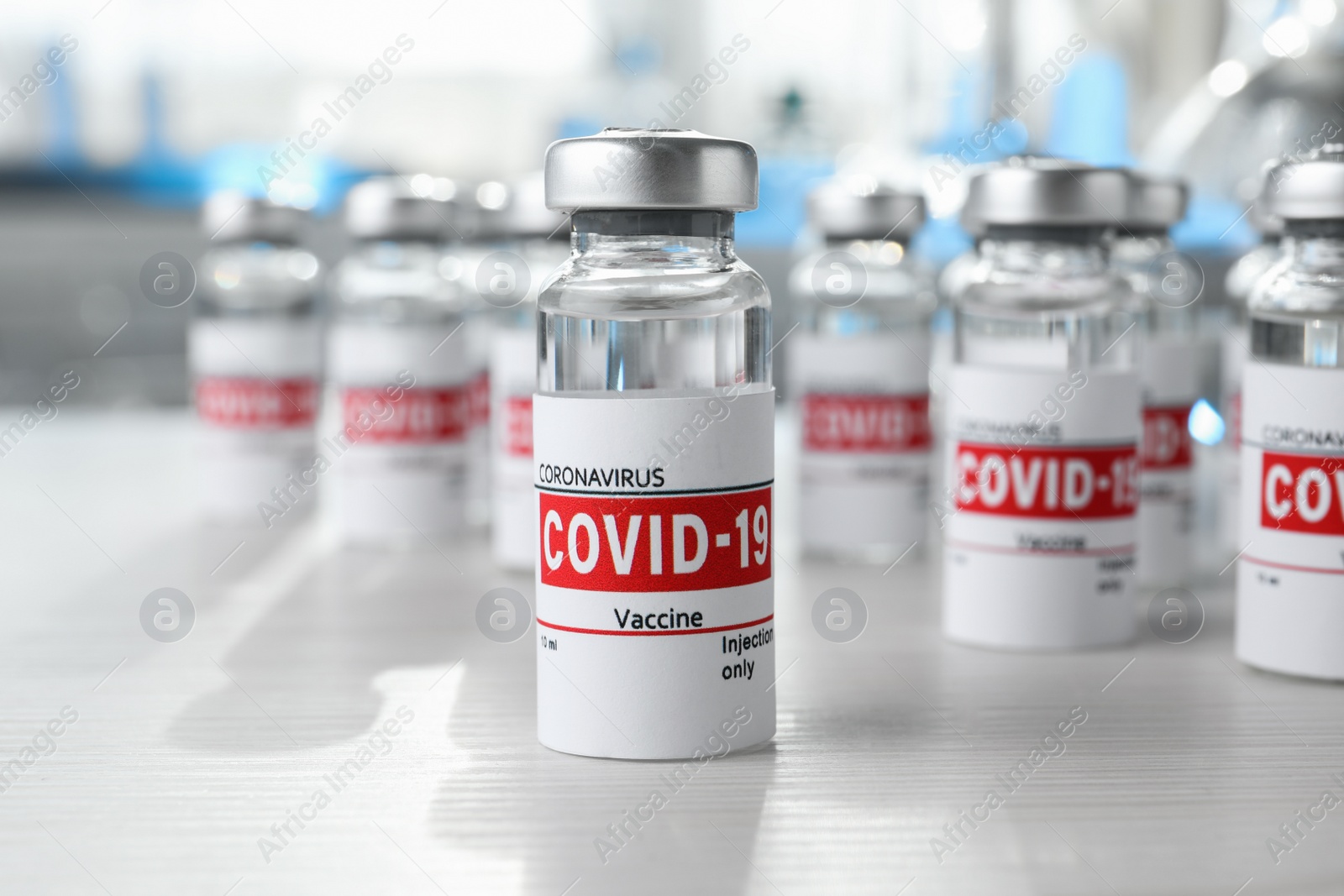 Photo of Glass vials with COVID-19 vaccine on white wooden table