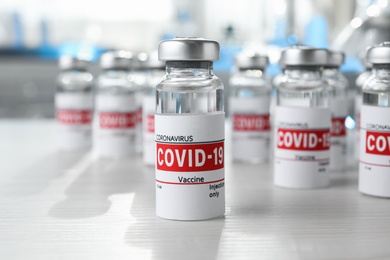 Photo of Glass vials with COVID-19 vaccine on white wooden table