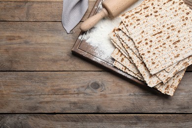 Photo of Stack of matzos and rolling pin on wooden table, flat lay. Space for text