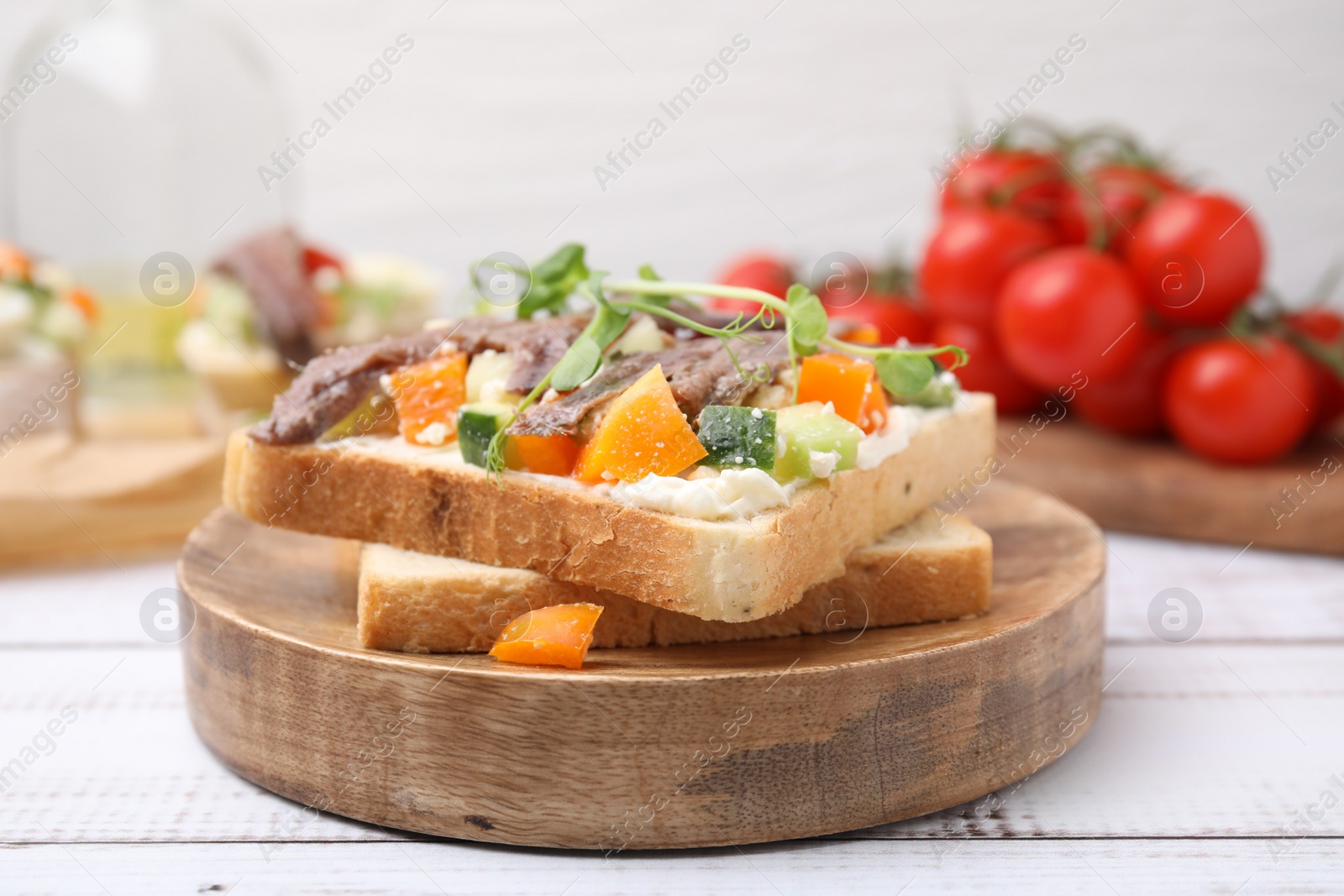 Photo of Delicious toasts with anchovies, cream cheese, bell peppers and cucumbers on white wooden table, closeup