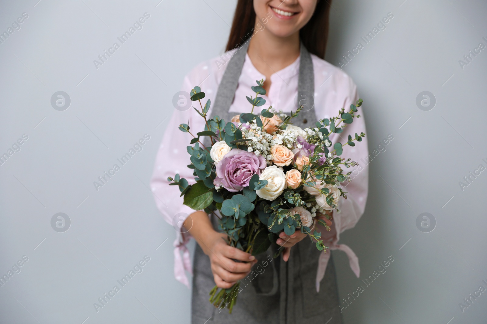 Photo of Florist holding beautiful wedding bouquet on light grey background, closeup