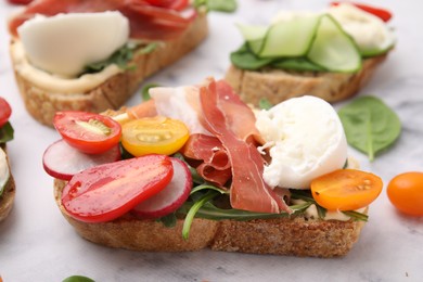 Photo of Delicious sandwich with burrata cheese, ham, radish and tomatoes on white table, closeup