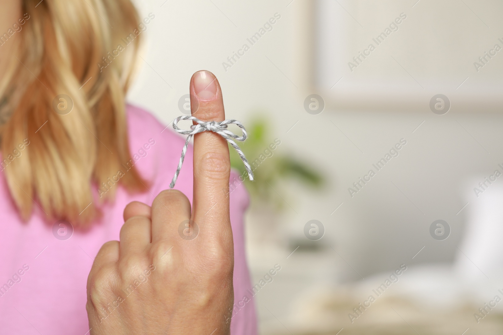 Photo of Woman showing index finger with tied bow as reminder on blurred background, closeup. Space for text