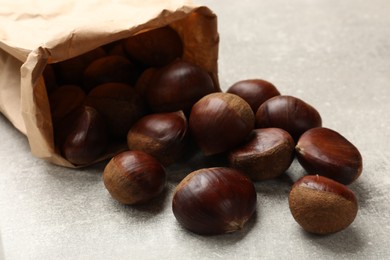 Photo of Paper bag with roasted edible sweet chestnuts on light grey table, closeup