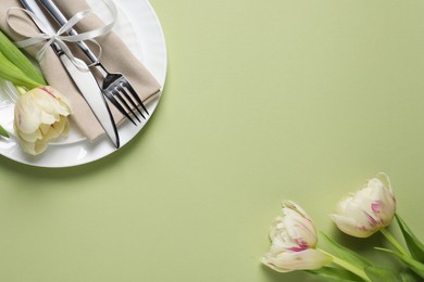 Photo of Stylish table setting with cutlery and tulips on light green background, flat lay. Space for text