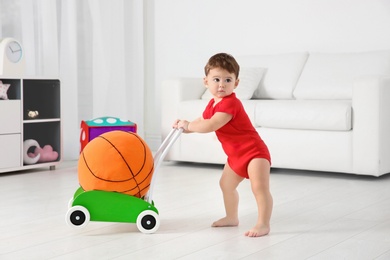 Cute baby playing with toy walker and ball at home
