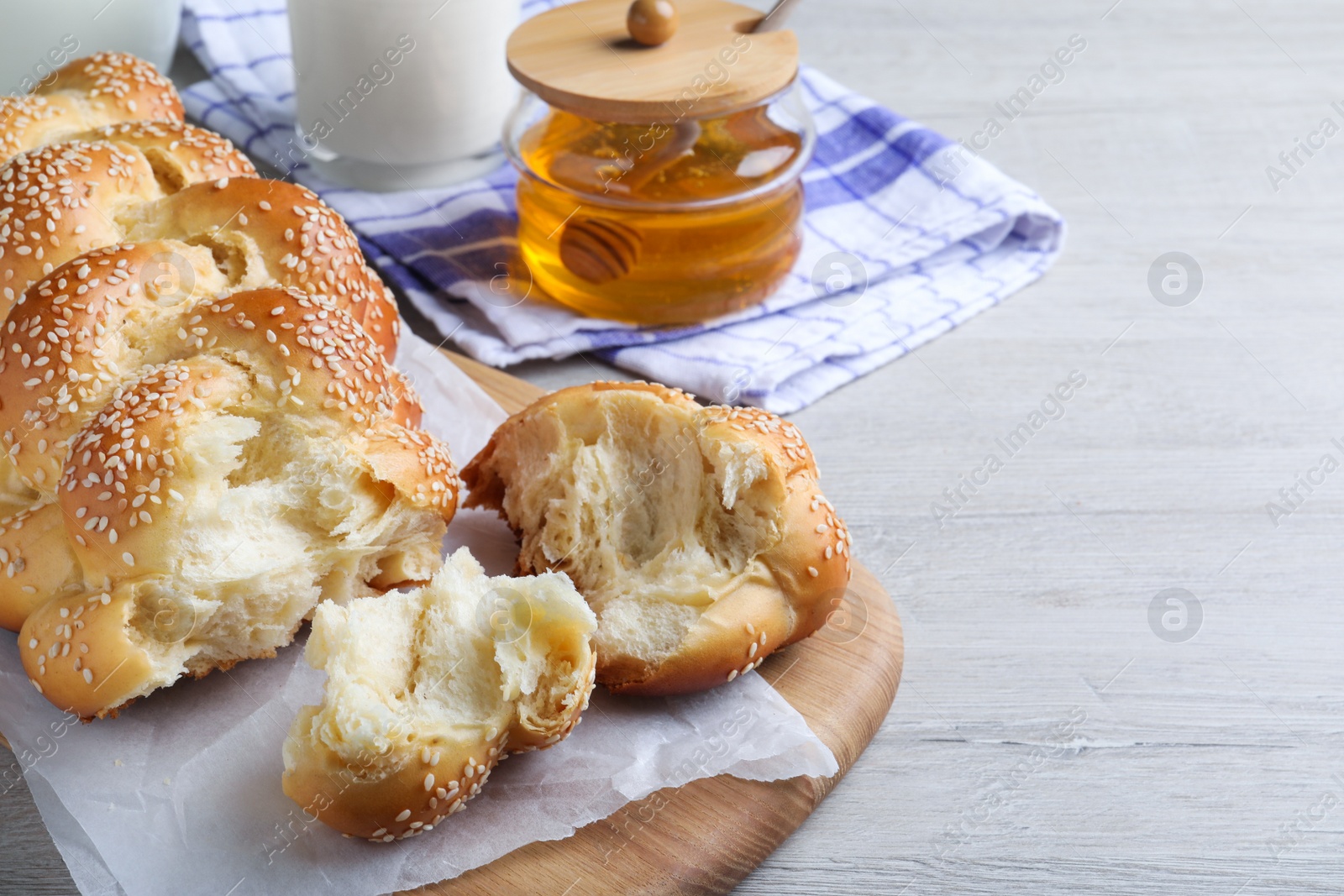 Photo of Broken homemade braided bread with sesame seeds on wooden table, space for text. Traditional Shabbat challah