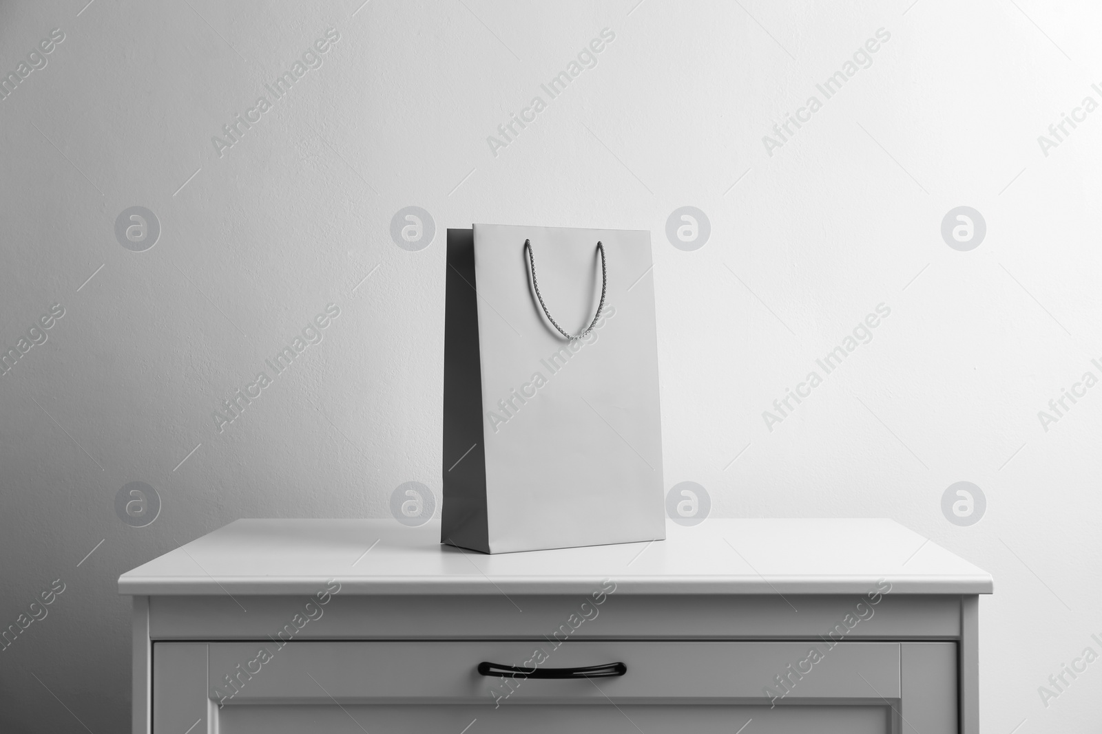 Photo of Paper shopping bag on white chest of drawers against light background