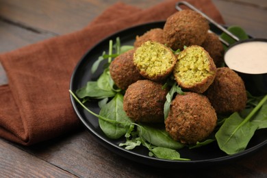 Photo of Delicious falafel balls, herbs and sauce on wooden table