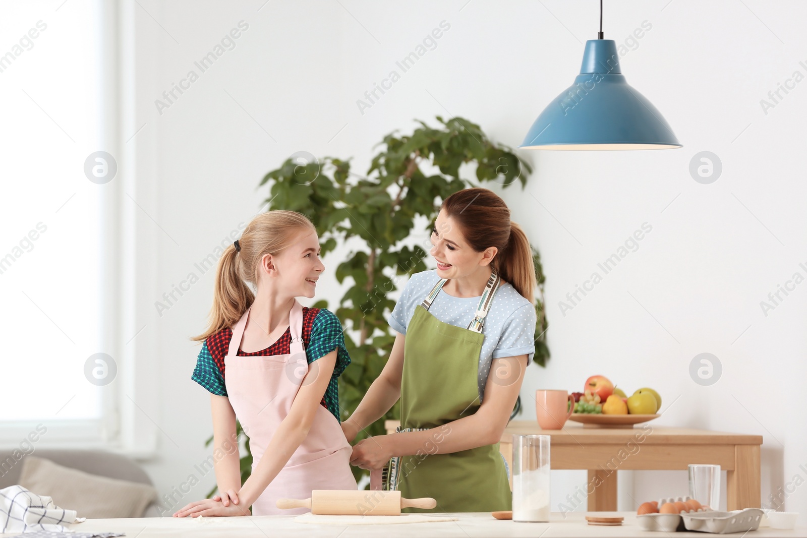 Photo of Mother and her daughter making dough at table in kitchen