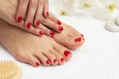 Photo of Woman showing stylish toenails after pedicure procedure and manicured hands with red polish on white terry towel, closeup