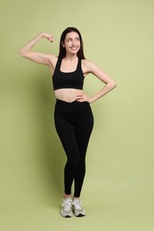 Photo of Happy young woman with slim body showing her muscles on green background