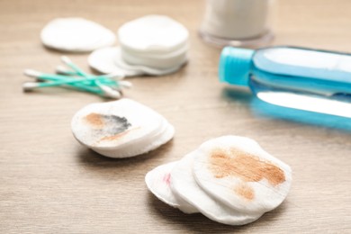 Photo of Dirty cotton pads and makeup removal product on wooden table, closeup