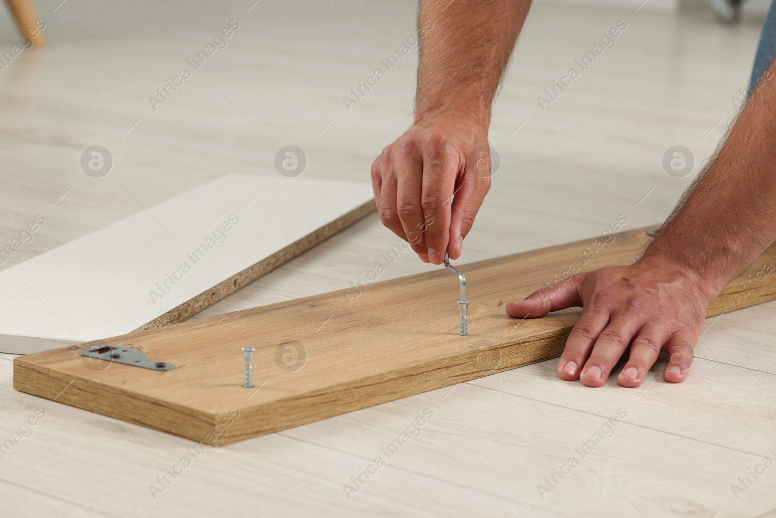 Photo of Man with hex key assembling furniture on floor indoors, closeup