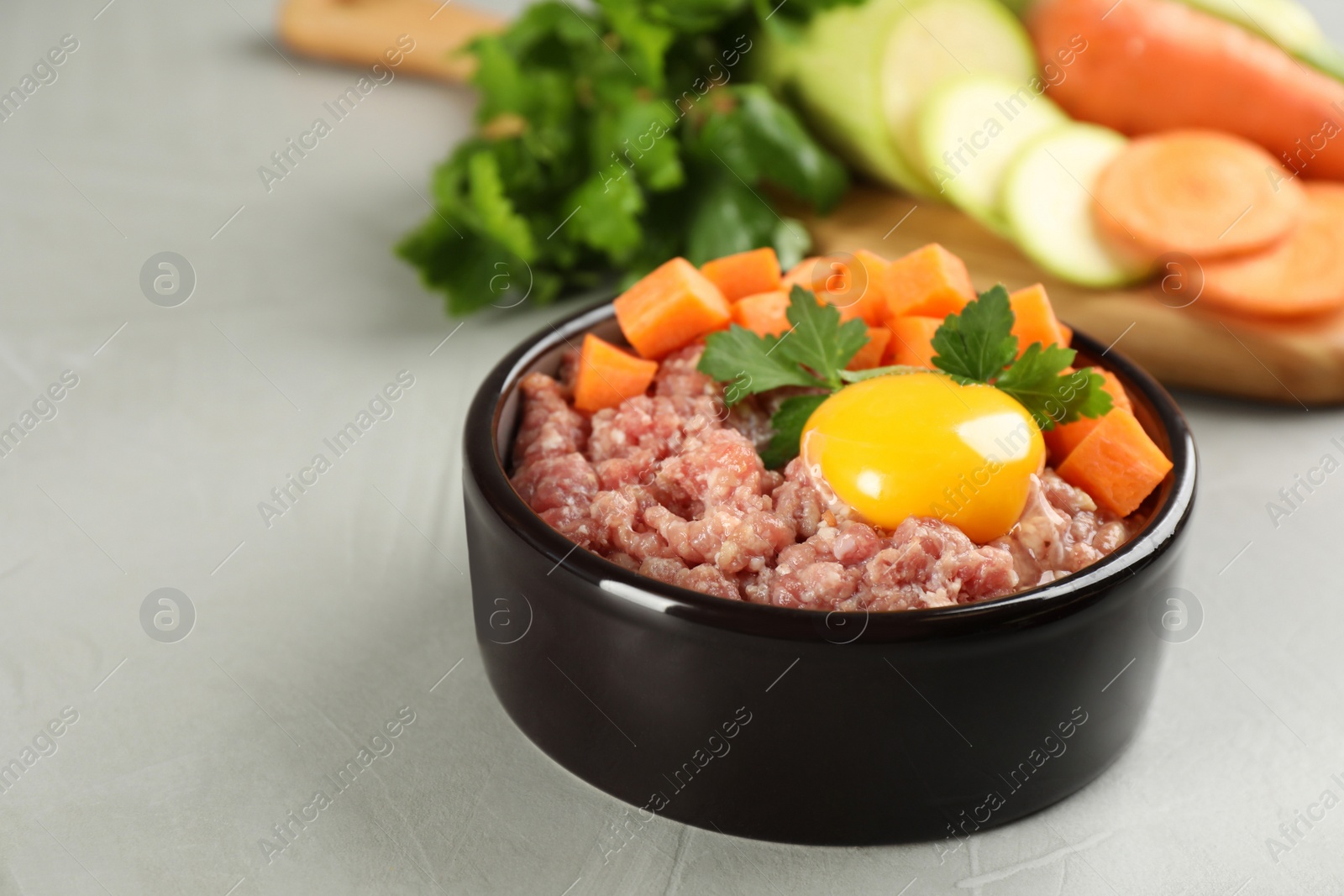 Photo of Natural pet food in feeding bowl on grey table, closeup. Space for text