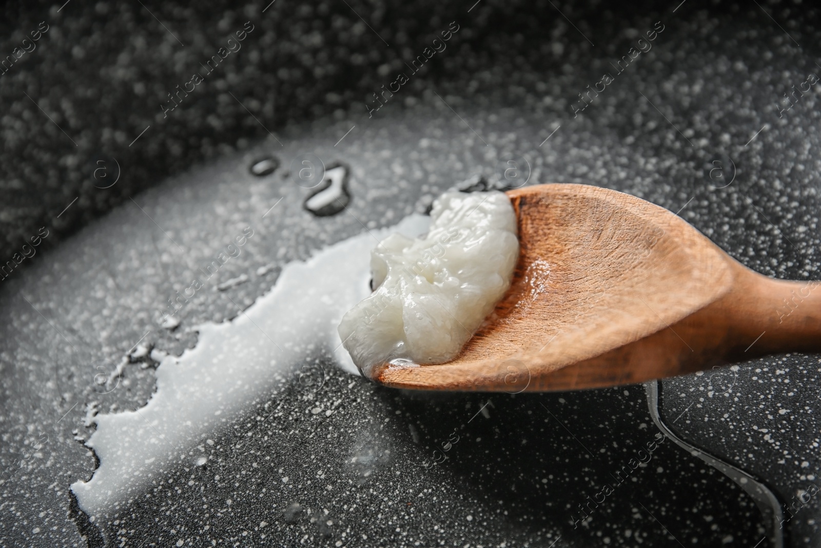 Photo of Wooden spoon with coconut oil in frying pan, closeup. Healthy cooking
