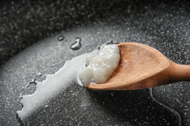 Wooden spoon with coconut oil in frying pan, closeup. Healthy cooking