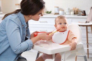 Mother feeding her cute little baby in kitchen