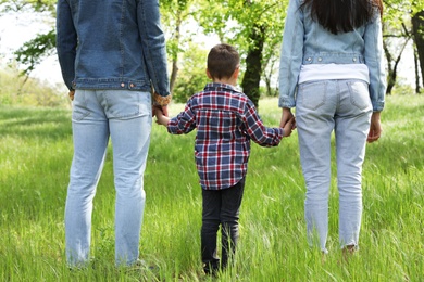 Photo of Little child holding hands with his parents in park. Family time