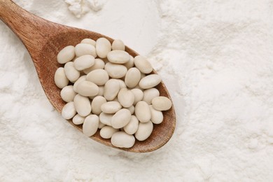 Wooden spoon with white kidney beans on flour, top view. Space for text