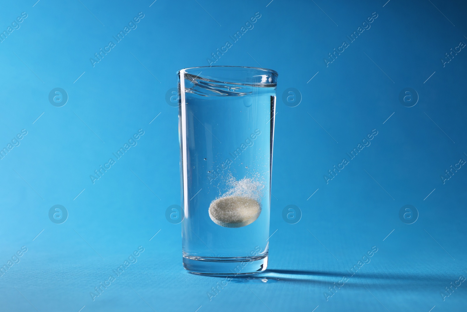 Photo of Effervescent pill dissolving in glass of water on light blue background