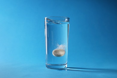 Photo of Effervescent pill dissolving in glass of water on light blue background