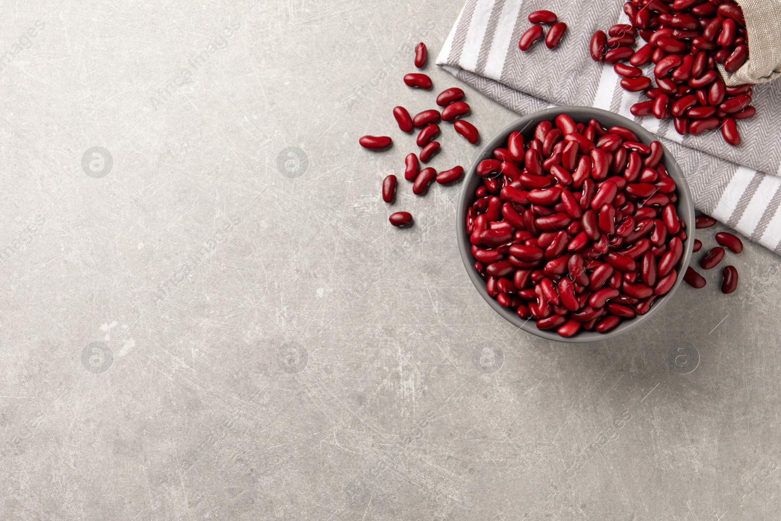 Photo of Raw red kidney beans with bowl and napkin on light grey table, flat lay. Space for text