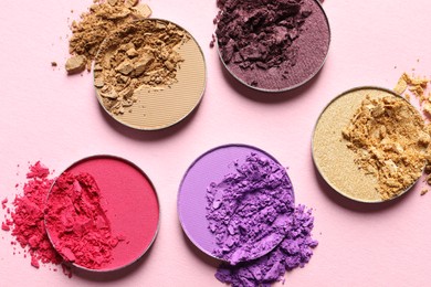 Photo of Different crushed eye shadows on pink background, flat lay