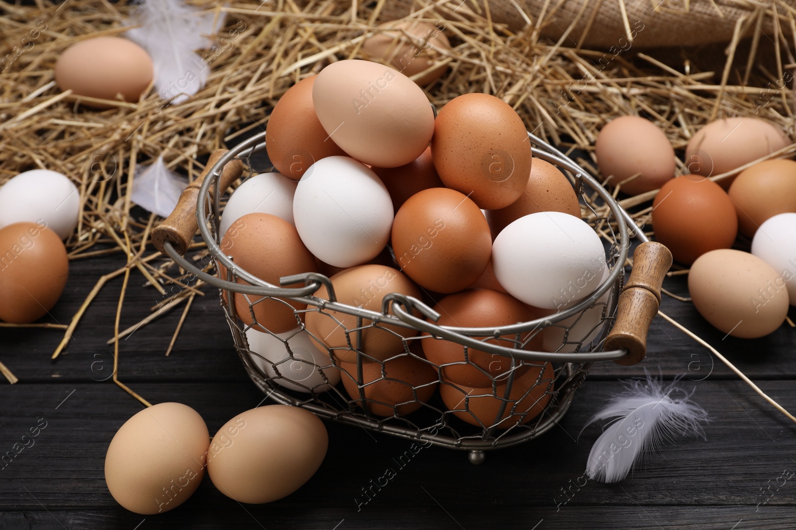 Photo of Fresh chicken eggs and dried straw on black wooden table