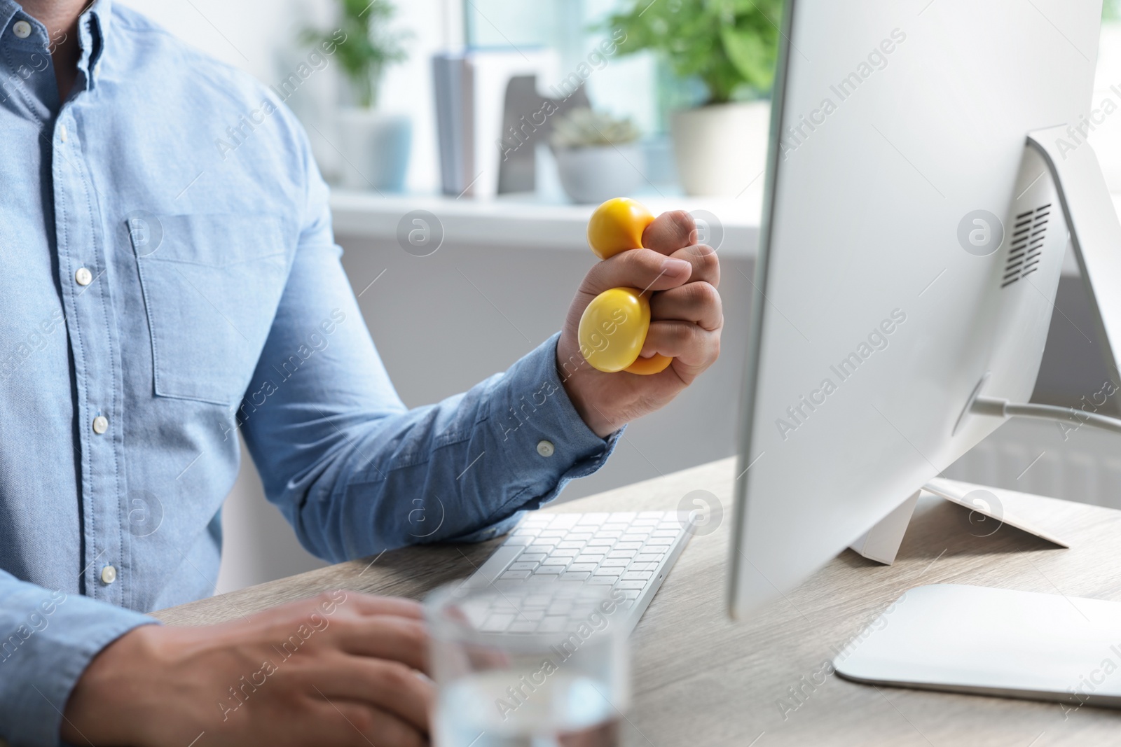 Photo of Man squeezing antistress ball while working with computer in office, closeup