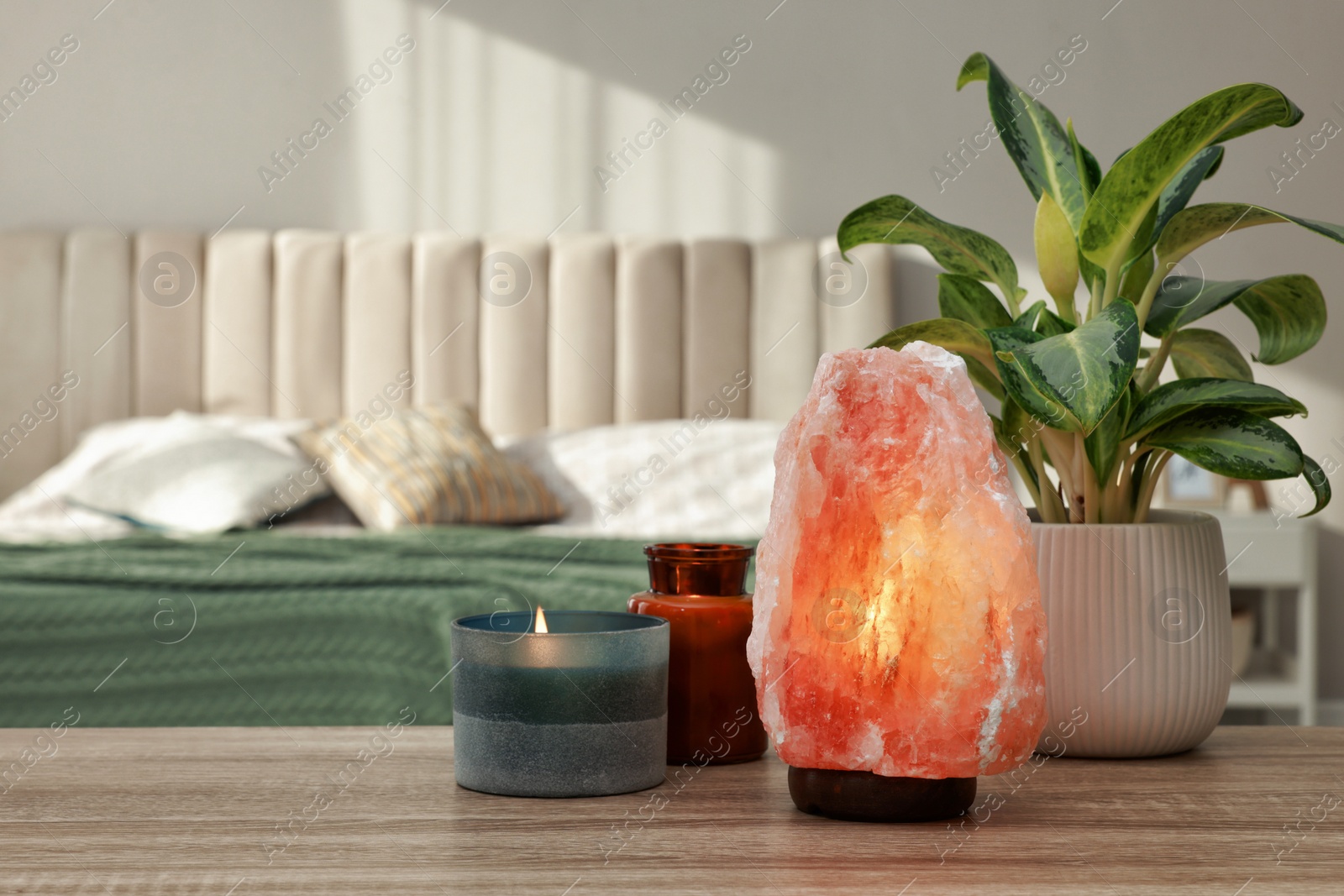Photo of Beautiful Himalayan salt lamp, green plant and candles on wooden table in bedroom, space for text