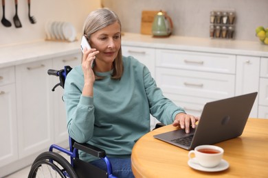 Photo of Woman in wheelchair talking on smartphone while using laptop at home