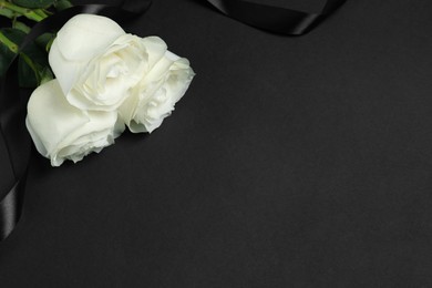 Photo of Beautiful roses and ribbon on black background, space for text. Funeral symbols
