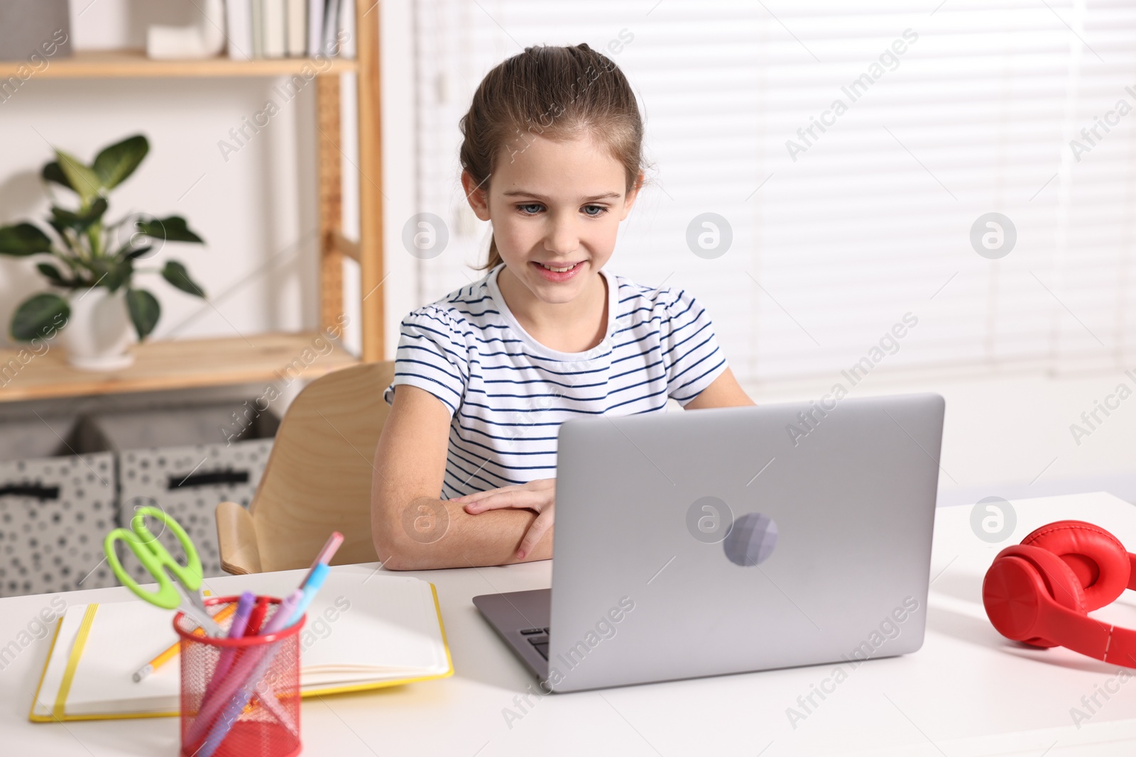 Photo of E-learning. Cute girl using laptop during online lesson at table indoors