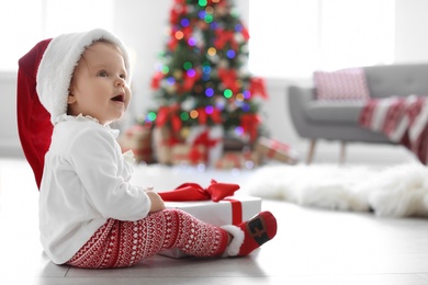 Cute baby in Santa hat with Christmas gift at home